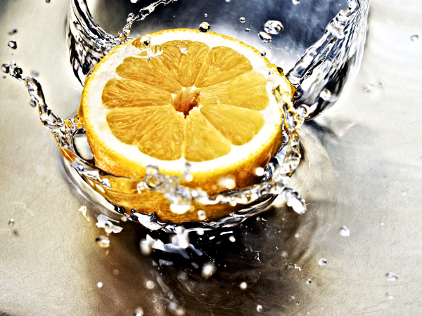 half a juicy lemon dropping into water, splashing out of the glass